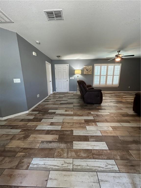 interior space featuring ceiling fan, a textured ceiling, baseboards, and visible vents