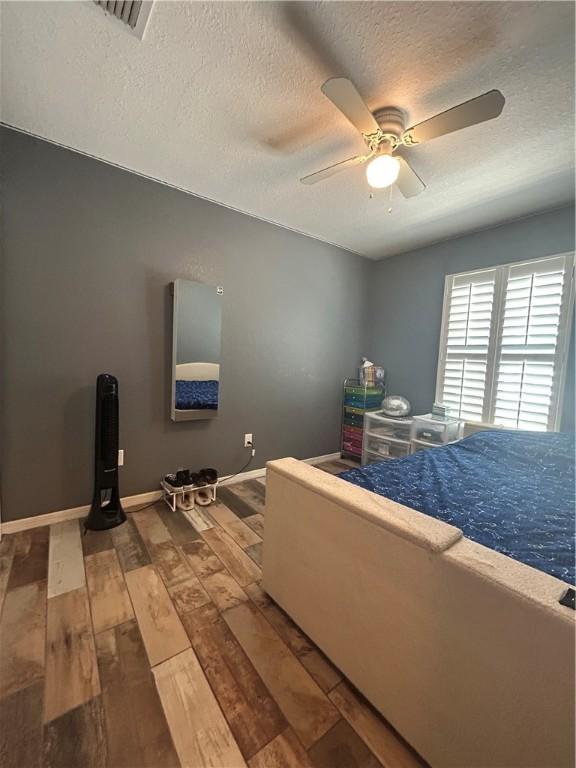 bedroom featuring baseboards, hardwood / wood-style floors, ceiling fan, and a textured ceiling
