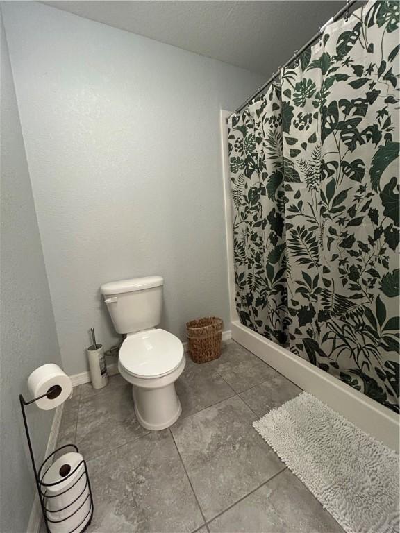 full bath featuring toilet, a shower with shower curtain, and baseboards