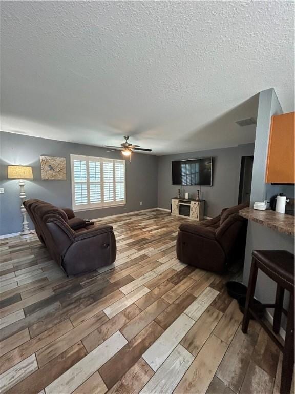 living area with a textured ceiling, a ceiling fan, visible vents, and light wood-style floors