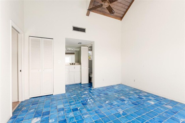 unfurnished bedroom with high vaulted ceiling, beam ceiling, ceiling fan, ensuite bath, and a closet