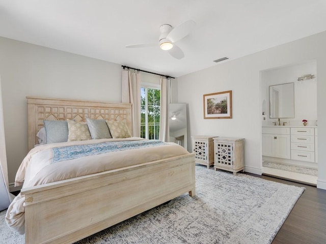 bedroom featuring ensuite bathroom, wood finished floors, visible vents, baseboards, and a ceiling fan