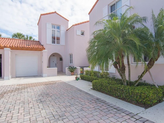 mediterranean / spanish home with a garage, decorative driveway, a tiled roof, and stucco siding