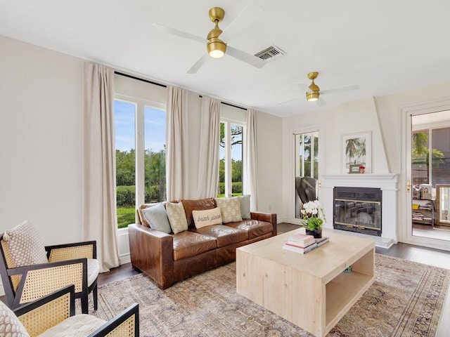 living room featuring light wood-style flooring, a fireplace, a ceiling fan, and a wealth of natural light