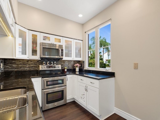 kitchen featuring dark wood-style flooring, dark countertops, decorative backsplash, appliances with stainless steel finishes, and white cabinetry