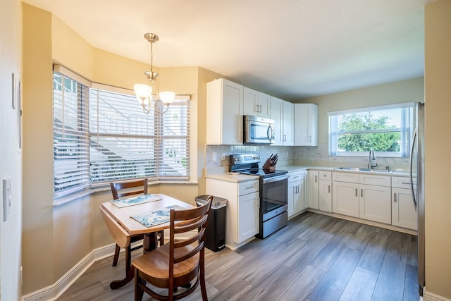 kitchen with light hardwood / wood-style floors, stainless steel appliances, white cabinets, hanging light fixtures, and sink