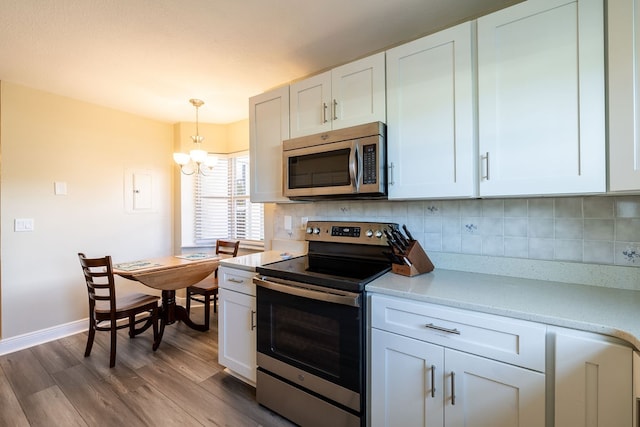 kitchen with tasteful backsplash, stainless steel appliances, white cabinetry, pendant lighting, and light hardwood / wood-style flooring