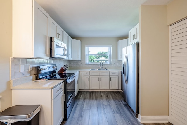 kitchen with wood-type flooring, backsplash, appliances with stainless steel finishes, sink, and white cabinets