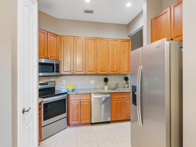 kitchen with light stone counters, appliances with stainless steel finishes, light tile patterned flooring, and sink