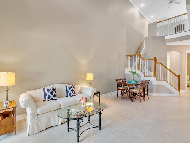 living room with ceiling fan, a towering ceiling, ornamental molding, and light tile patterned floors