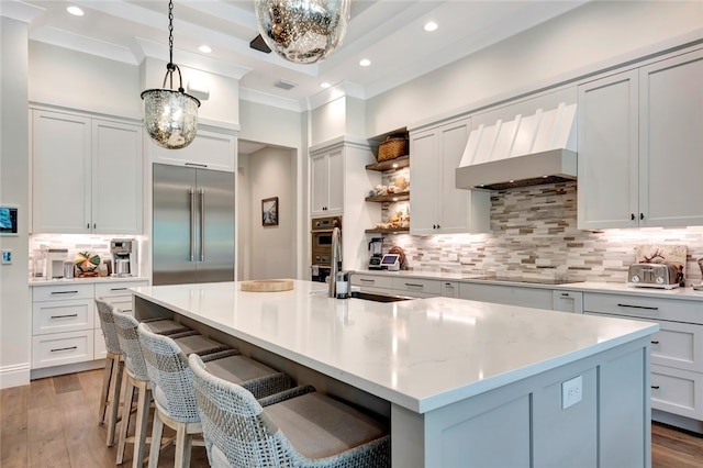 kitchen with hardwood / wood-style flooring, appliances with stainless steel finishes, a center island with sink, and decorative light fixtures