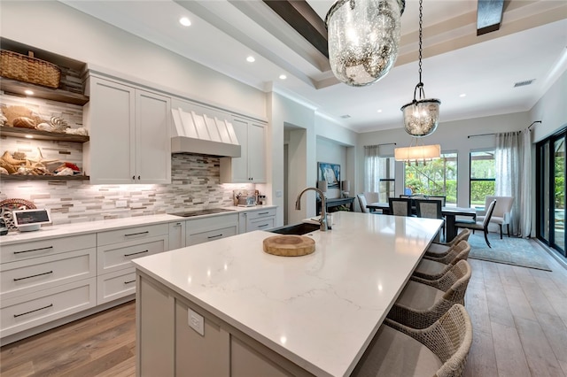 kitchen featuring tasteful backsplash, light wood-type flooring, hanging light fixtures, and a center island with sink