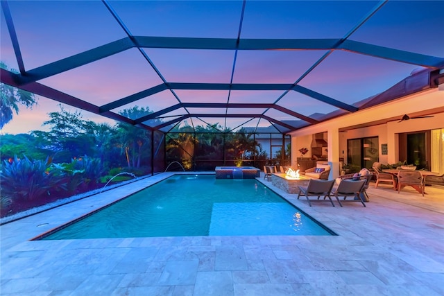 pool at dusk with glass enclosure, pool water feature, a patio, ceiling fan, and an outdoor hangout area