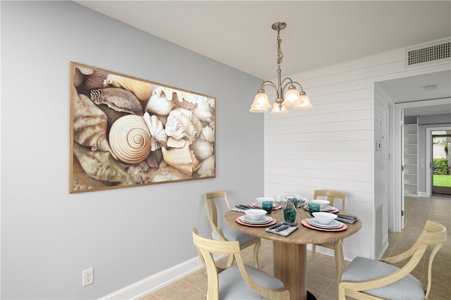 dining area featuring wooden walls, light tile patterned floors, and an inviting chandelier