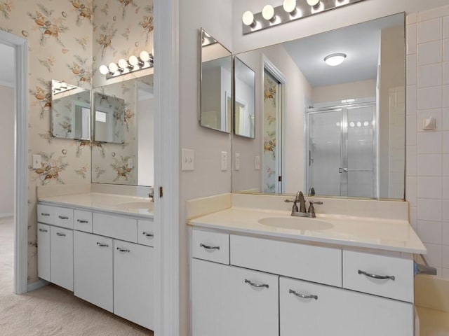 full bath featuring a sink, two vanities, a shower stall, and wallpapered walls