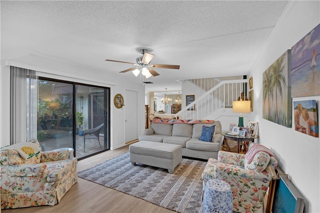 living room featuring light hardwood / wood-style floors, ceiling fan with notable chandelier, and a textured ceiling