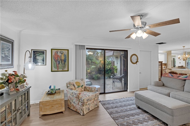 living room featuring ceiling fan with notable chandelier, light hardwood / wood-style flooring, and a textured ceiling