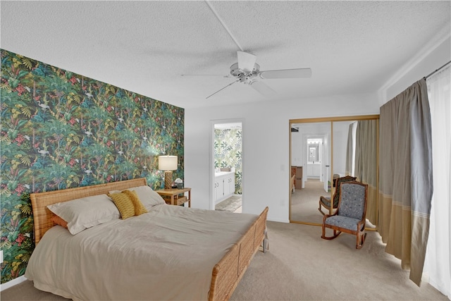 bedroom with ceiling fan, ensuite bath, a textured ceiling, and light colored carpet