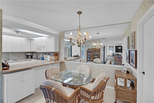 dining area with light tile patterned flooring, ceiling fan with notable chandelier, a textured ceiling, and sink