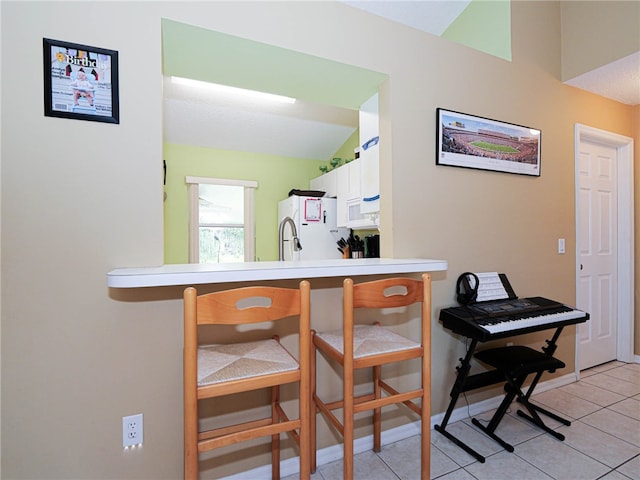 kitchen featuring light tile patterned flooring, white cabinets, a breakfast bar area, white appliances, and lofted ceiling