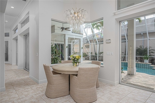 dining room with baseboards, ornamental molding, ceiling fan with notable chandelier, and a towering ceiling