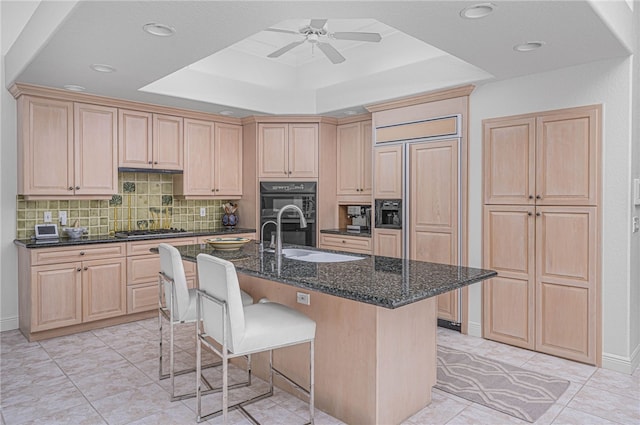 kitchen with a sink, paneled built in refrigerator, light brown cabinetry, and a breakfast bar