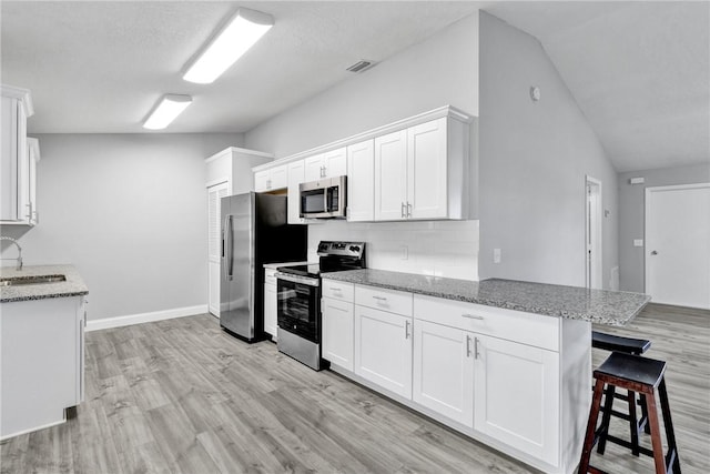 kitchen with a kitchen bar, appliances with stainless steel finishes, light stone countertops, white cabinets, and lofted ceiling