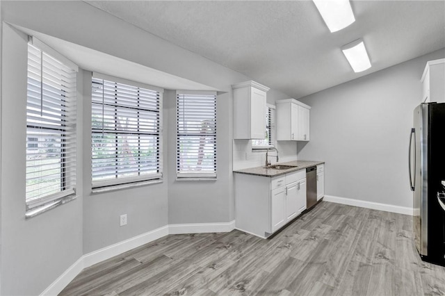 kitchen with white cabinets, sink, light hardwood / wood-style flooring, dark stone countertops, and stainless steel appliances