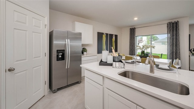 kitchen with stainless steel fridge with ice dispenser, light tile patterned floors, white cabinets, light countertops, and a sink