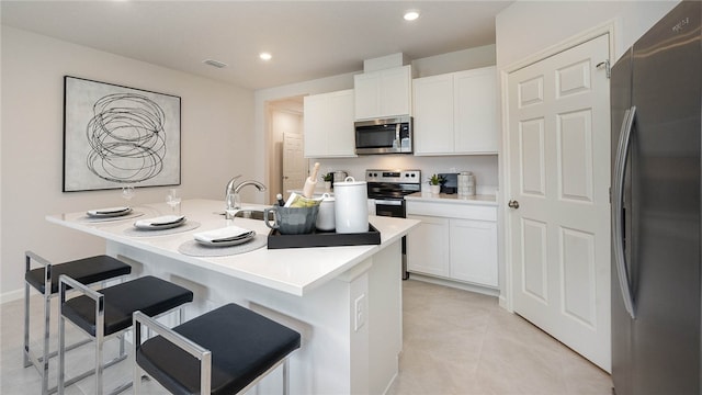 kitchen with a kitchen bar, a sink, white cabinets, and stainless steel appliances