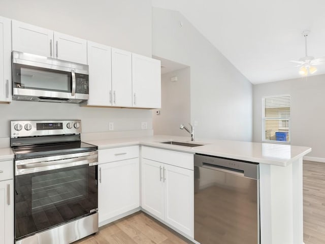 kitchen with appliances with stainless steel finishes, lofted ceiling, sink, white cabinets, and kitchen peninsula