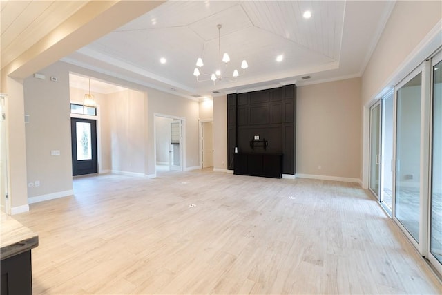 unfurnished living room featuring a tray ceiling, light wood-type flooring, baseboards, a notable chandelier, and crown molding