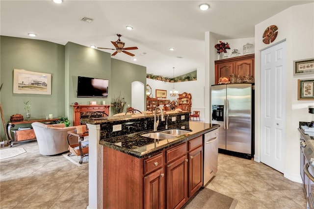 kitchen featuring visible vents, dark stone counters, appliances with stainless steel finishes, a sink, and ceiling fan with notable chandelier