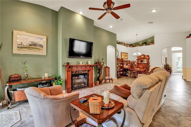 living area with arched walkways, a glass covered fireplace, lofted ceiling, ceiling fan with notable chandelier, and light tile patterned flooring