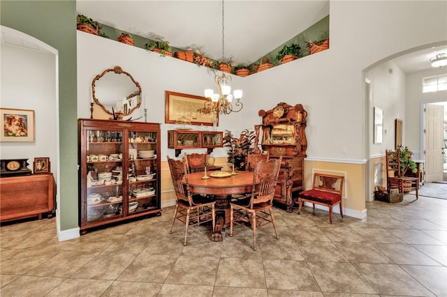 tiled dining room with baseboards, arched walkways, and a chandelier