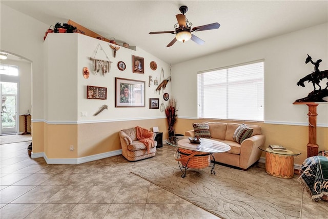 living area featuring arched walkways, vaulted ceiling, ceiling fan, tile patterned flooring, and baseboards