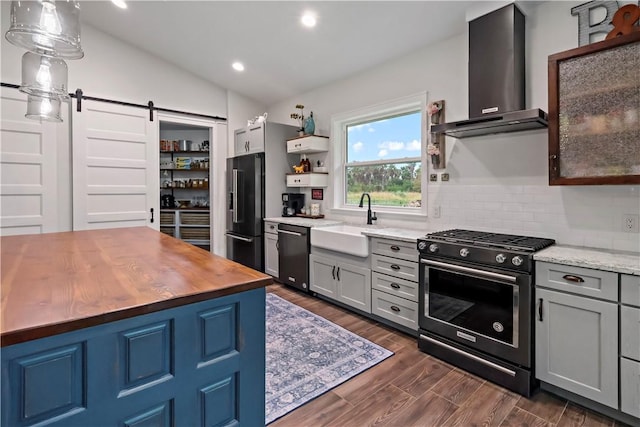 kitchen featuring appliances with stainless steel finishes, sink, wall chimney range hood, a barn door, and lofted ceiling