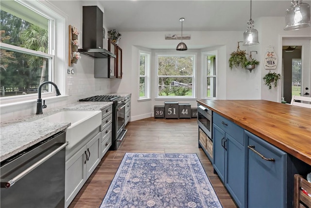 kitchen with backsplash, wooden counters, hanging light fixtures, wall chimney exhaust hood, and appliances with stainless steel finishes