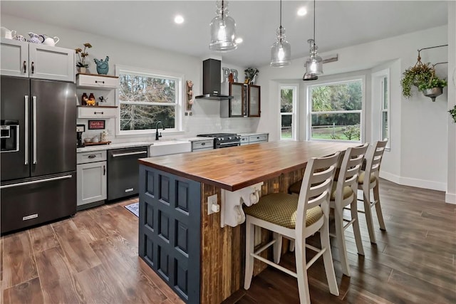 kitchen featuring pendant lighting, a center island, wall chimney range hood, dark hardwood / wood-style flooring, and stainless steel appliances