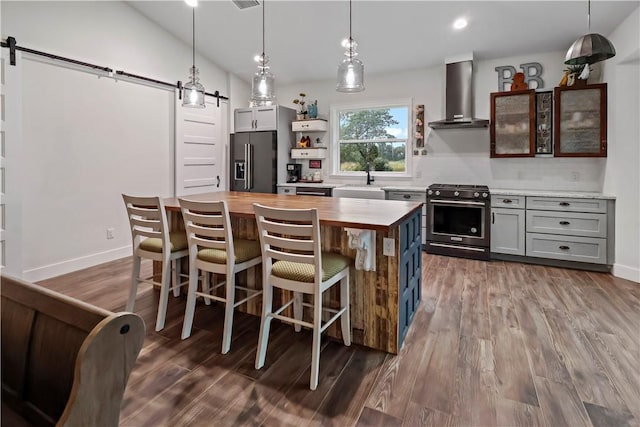 kitchen with a barn door, hanging light fixtures, wall chimney range hood, and appliances with stainless steel finishes