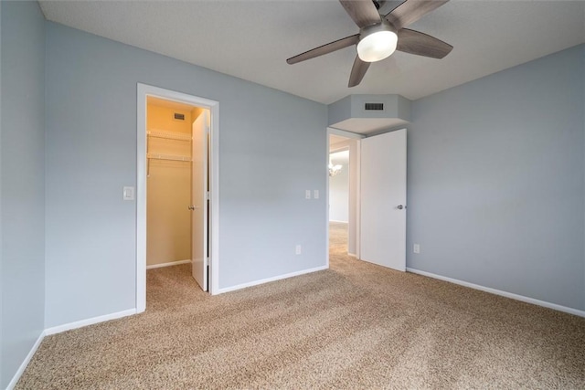 unfurnished bedroom featuring ceiling fan, a walk in closet, a closet, and carpet