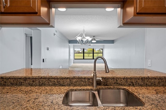 kitchen with ceiling fan with notable chandelier, sink, a textured ceiling, and stone counters