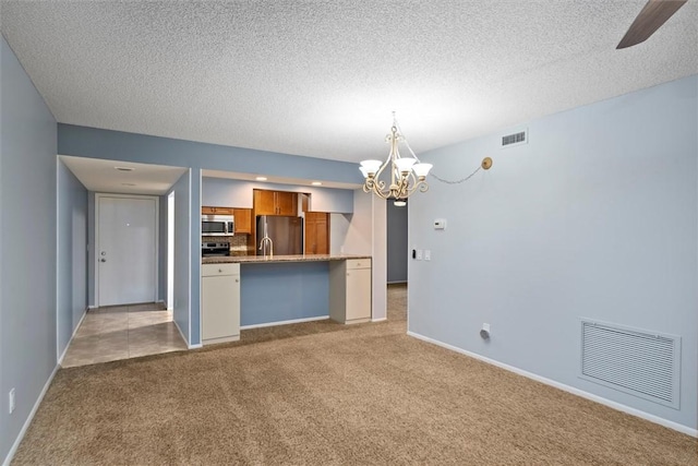 kitchen with a textured ceiling, decorative light fixtures, light carpet, stainless steel appliances, and a notable chandelier