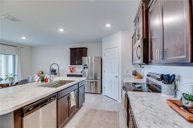 kitchen with a kitchen breakfast bar, stainless steel appliances, a kitchen island with sink, sink, and light tile patterned floors