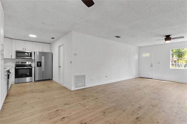 kitchen featuring appliances with stainless steel finishes, a textured ceiling, light hardwood / wood-style floors, and white cabinetry