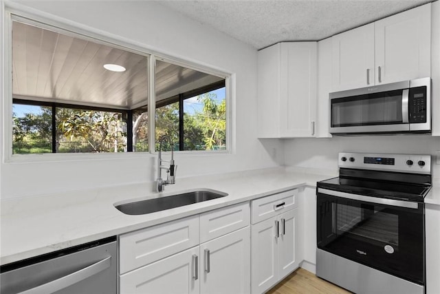 kitchen with a textured ceiling, stainless steel appliances, a healthy amount of sunlight, sink, and white cabinets