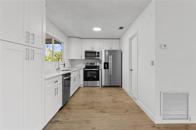 kitchen with appliances with stainless steel finishes, a textured ceiling, sink, light hardwood / wood-style flooring, and white cabinetry