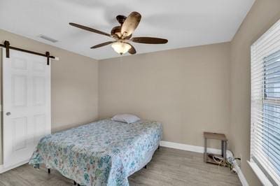 bedroom featuring hardwood / wood-style flooring, a barn door, and ceiling fan