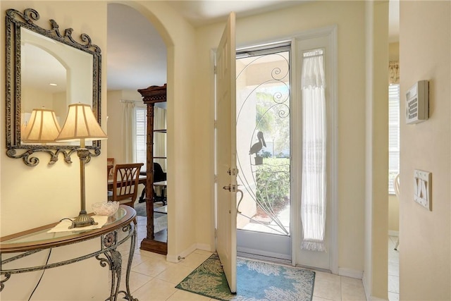 entryway with light tile patterned floors, a healthy amount of sunlight, arched walkways, and baseboards