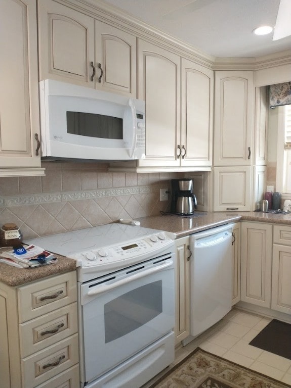 kitchen featuring cream cabinetry, decorative backsplash, white appliances, and light tile patterned flooring